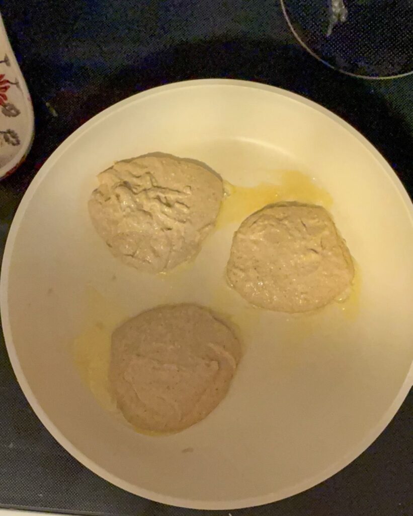 Three pancakes cooking a skillet before they have been flipped.