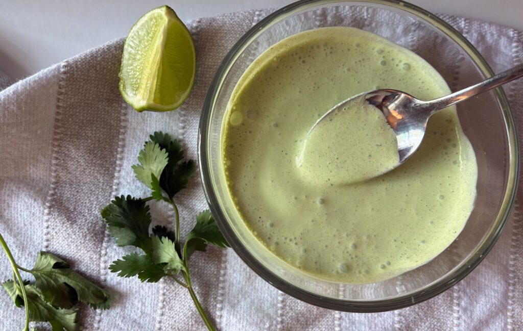 Cilantro lime sauce in a bowl with a lime and cilantro leaves laying next to the bowl