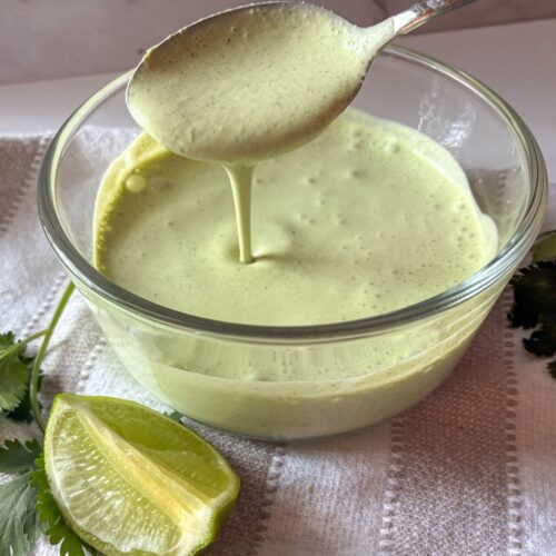 A spoon drizzling sour cream cilantro lime sauce into a bowl