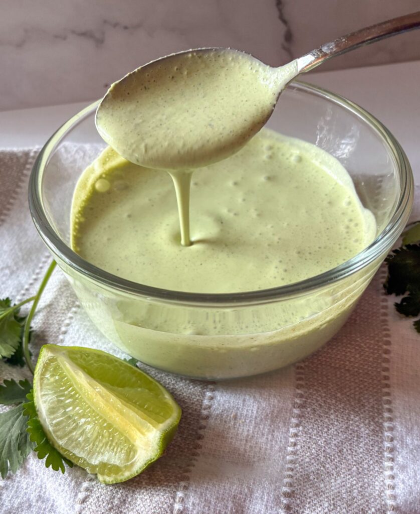 A spoon drizzling sour cream cilantro lime sauce into a bowl