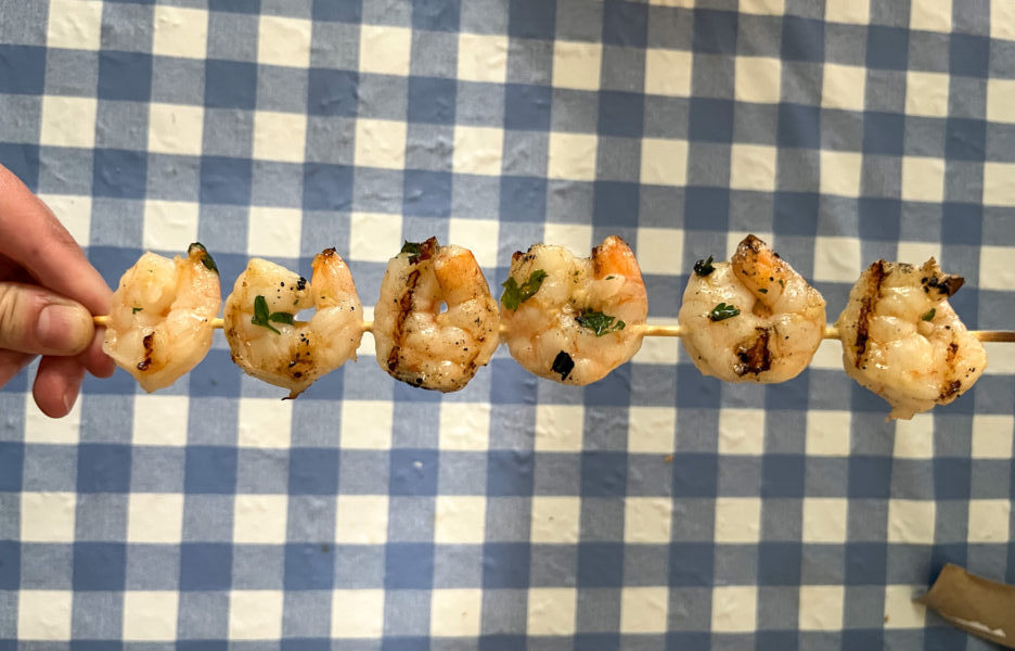 person holding 1 grilled shrimp on a skewer