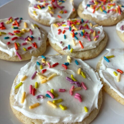 seven eggless sugar cookies displayed on a plate with icing and sprinkles