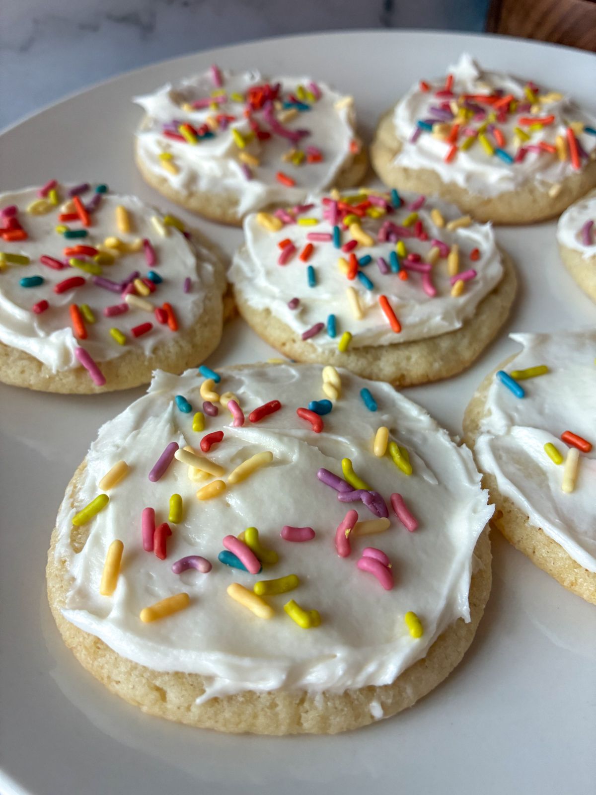 seven eggless sugar cookies displayed on a plate with icing and sprinkles