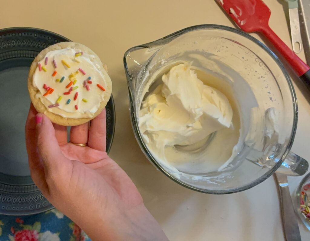 Frosting in a large bowl and a hand holding a cookie with frosting on it