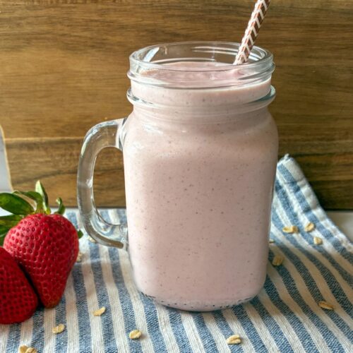 strawberry oatmeal smoothie served in a glass with strawberries on the side and a straw in the cup