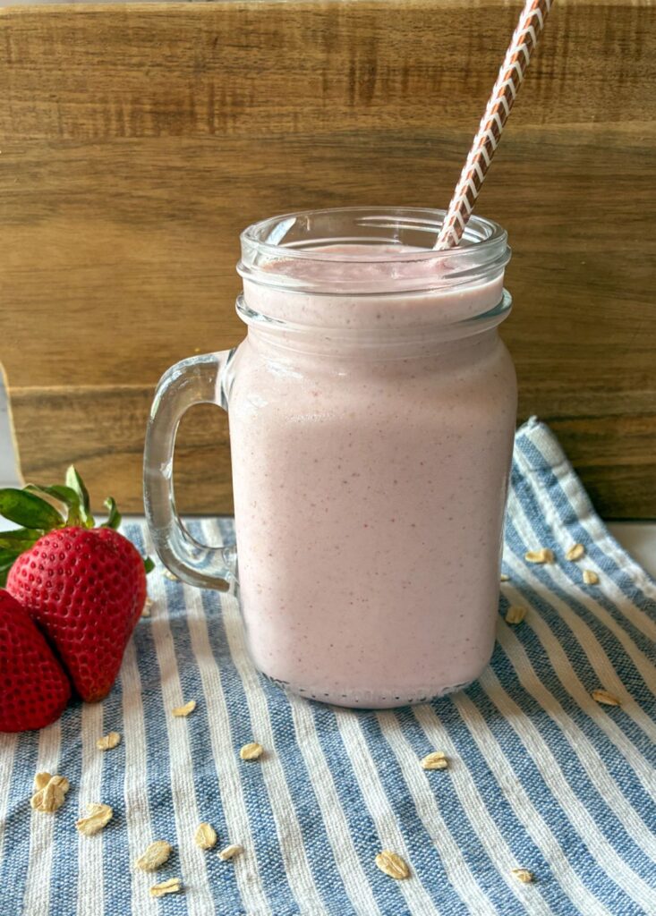 strawberry oatmeal smoothie served in a glass with strawberries on the side and a straw in the cup