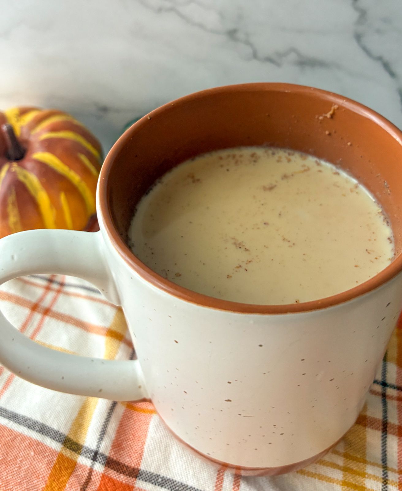 Pumpkin chai tea latte served in a mug with a little pumpkin sitting next to it