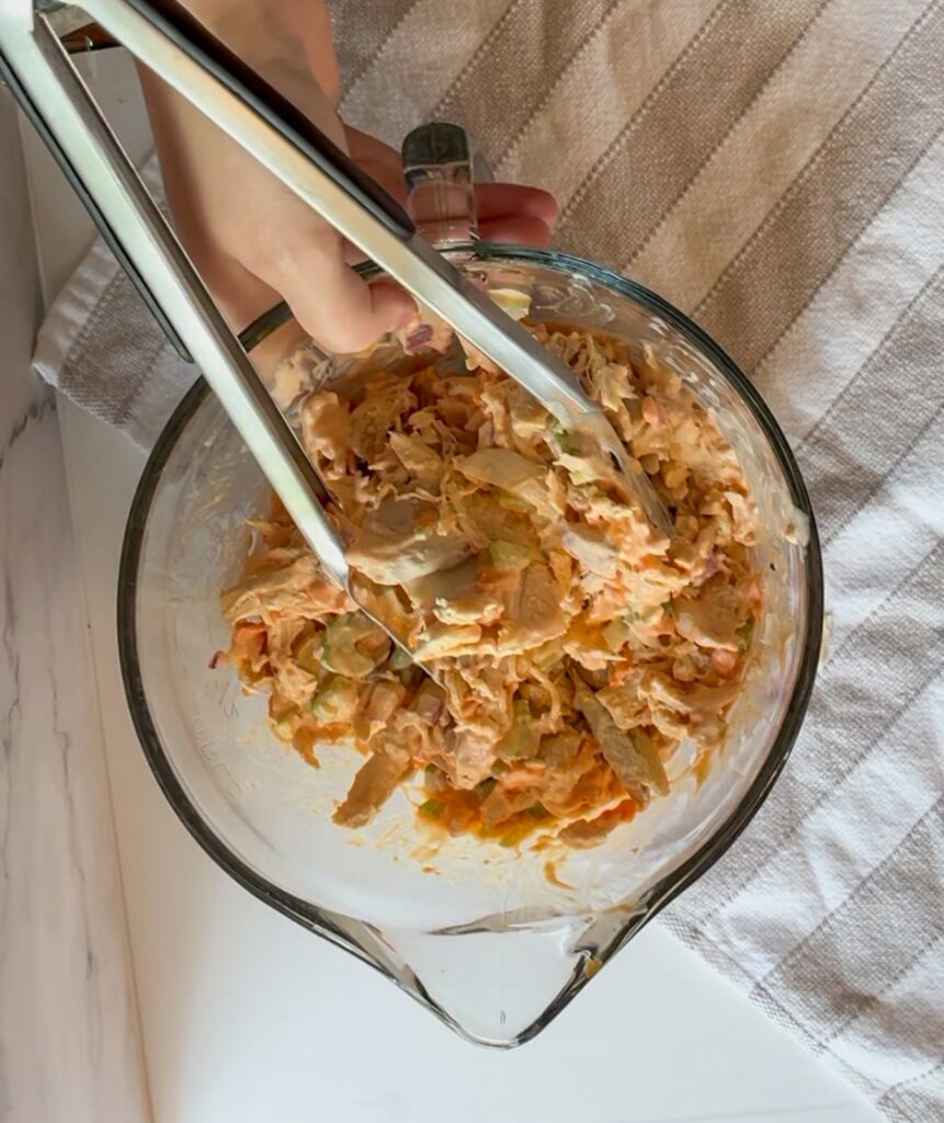 buffalo chicken salad in a large bowl with serving tongs