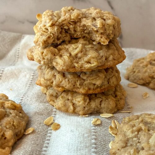A stack of eggless oatmeal cookies and the one has a bite out of it.