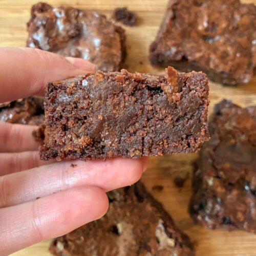 A hand holding the brownie above a plate filled with more brownies