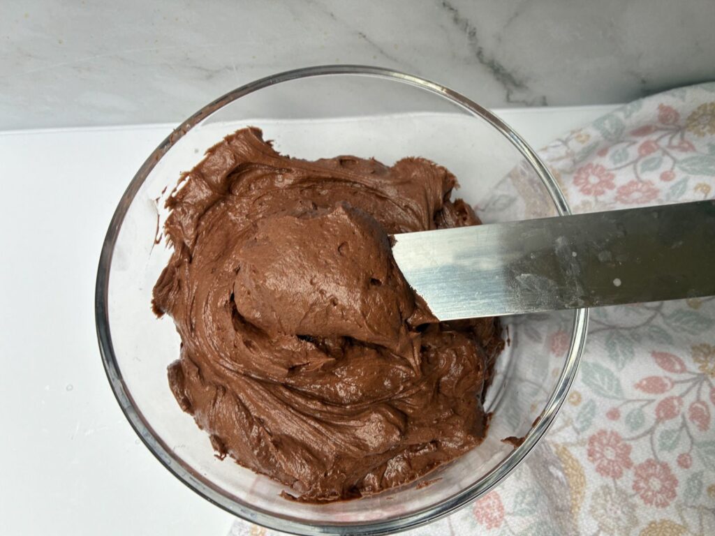 chocolate buttercream frosting being scooped out of a bowl