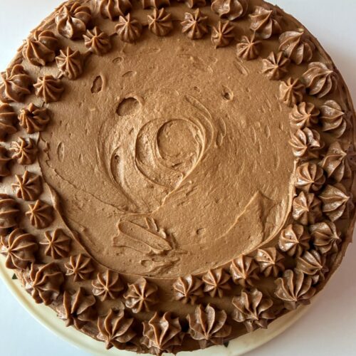frosting cake with piping along the outside with the chocolate buttercream frosting