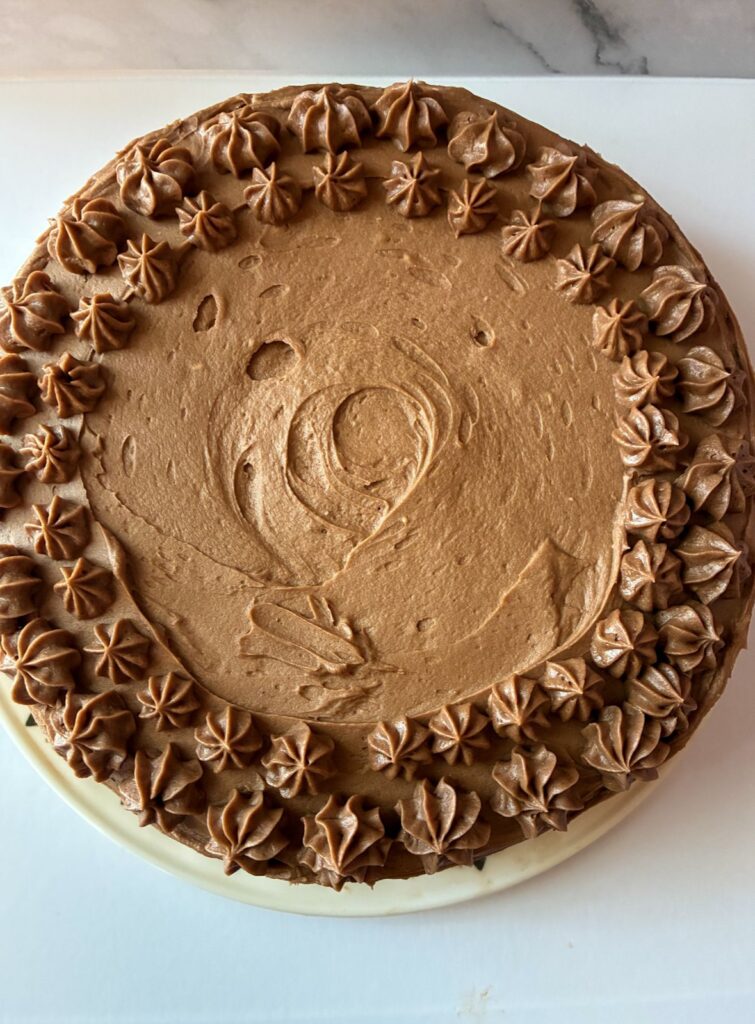 frosting cake with piping along the outside with the chocolate buttercream frosting