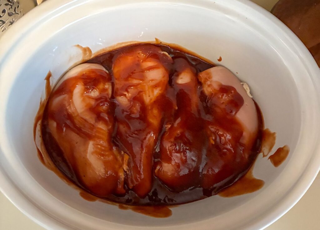 Raw chicken covered in sauce inside of a slow cooker