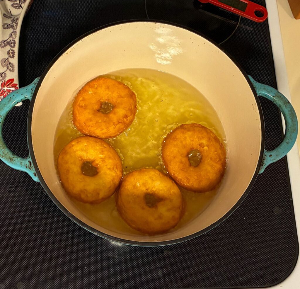 4 canned biscuit donuts almost done cooking in a large Dutch oven