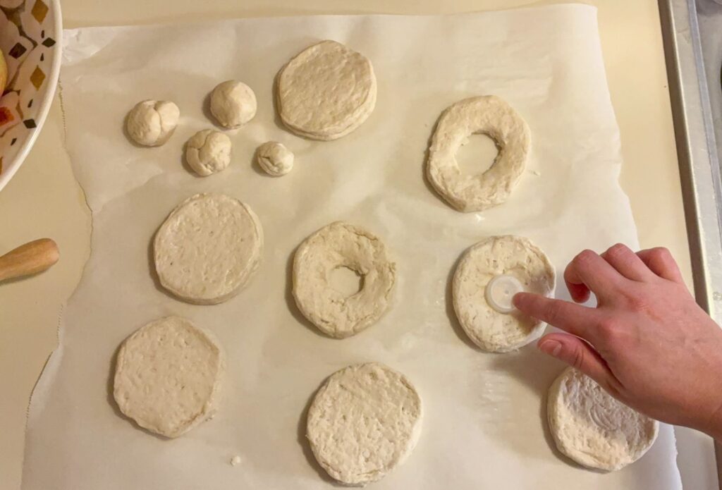 8 biscuits laid out on parchment paper with a hand cutting out the center holes