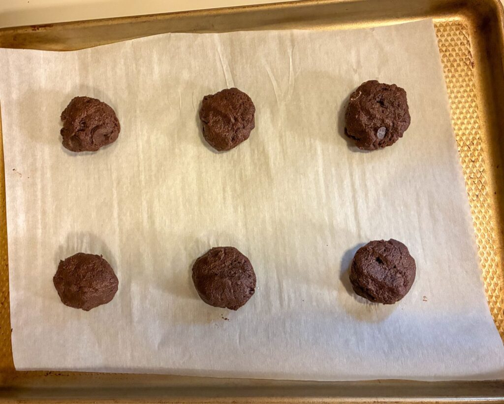 A parchment lined baking sheet with 6 dough balls spaced 3 inches apart