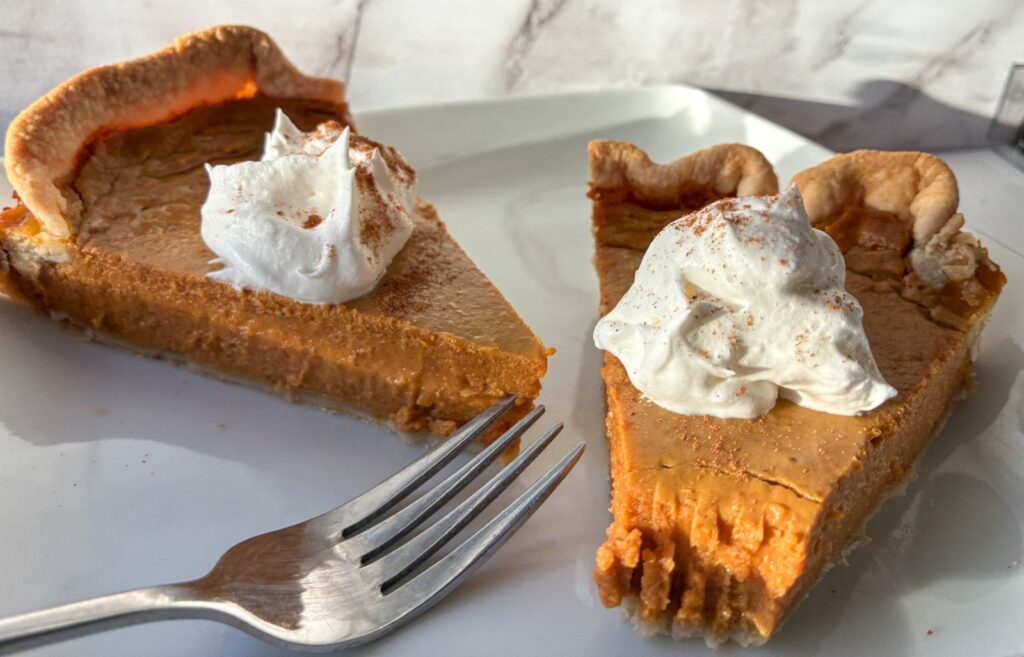 Two pieces of eggless pumpkin pie on a plate with a fork next to them