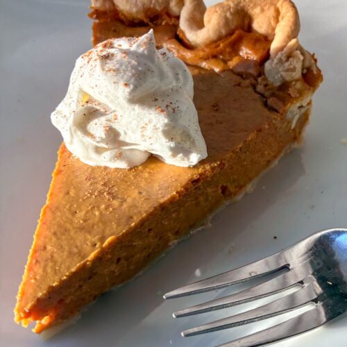 eggless pumpkin pie on a plate with whipped cream and a fork next to it