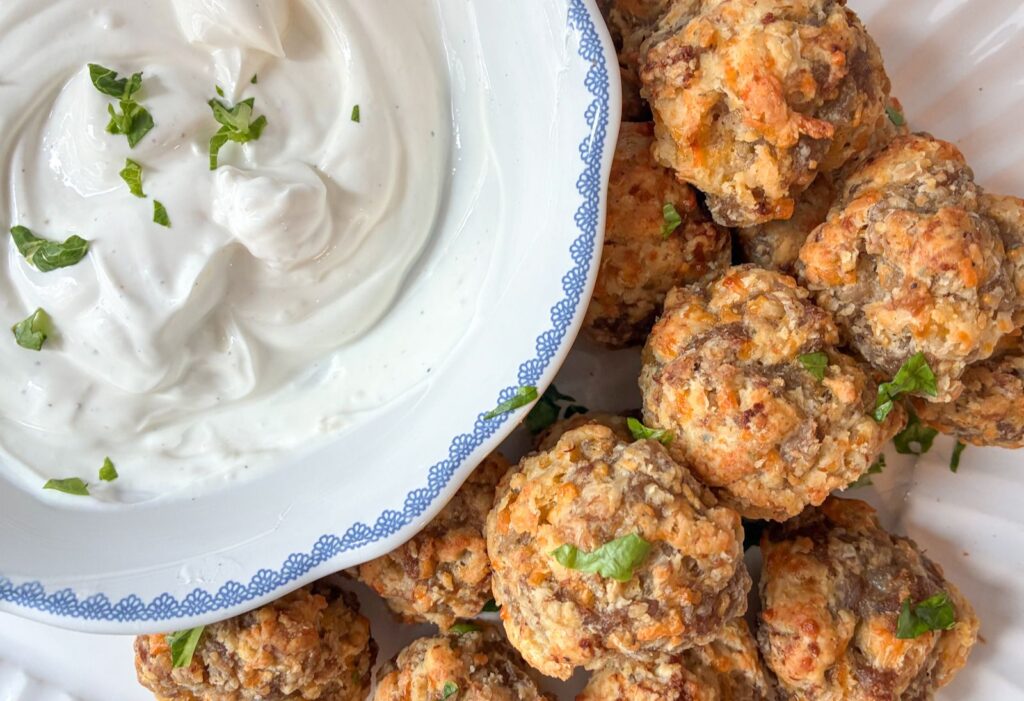 Sausage balls in a pile with a bowl of garlic dip next to it