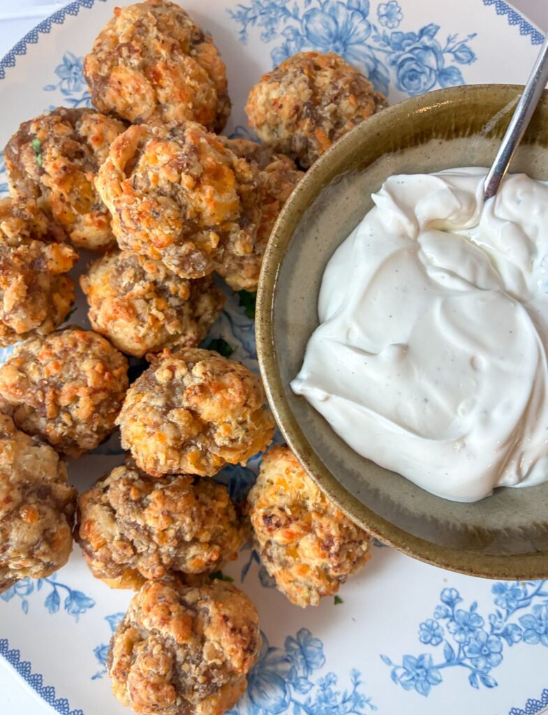 Sausage balls served on a plate with a bowl of dipping sauce next to it