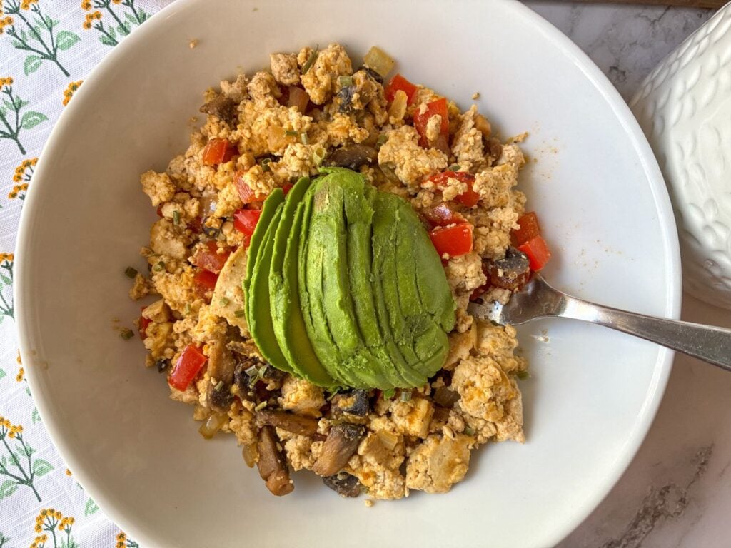 Tofu scramble with mushrooms and peppers served in a bowl and topped with a sliced avocado