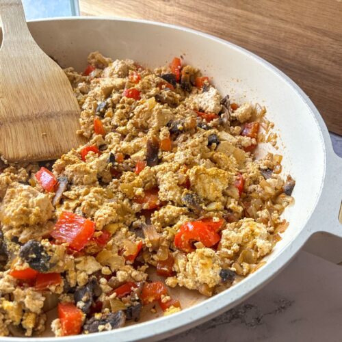 Tofu scramble with mushrooms and peppers in a large skillet with a serving spoon