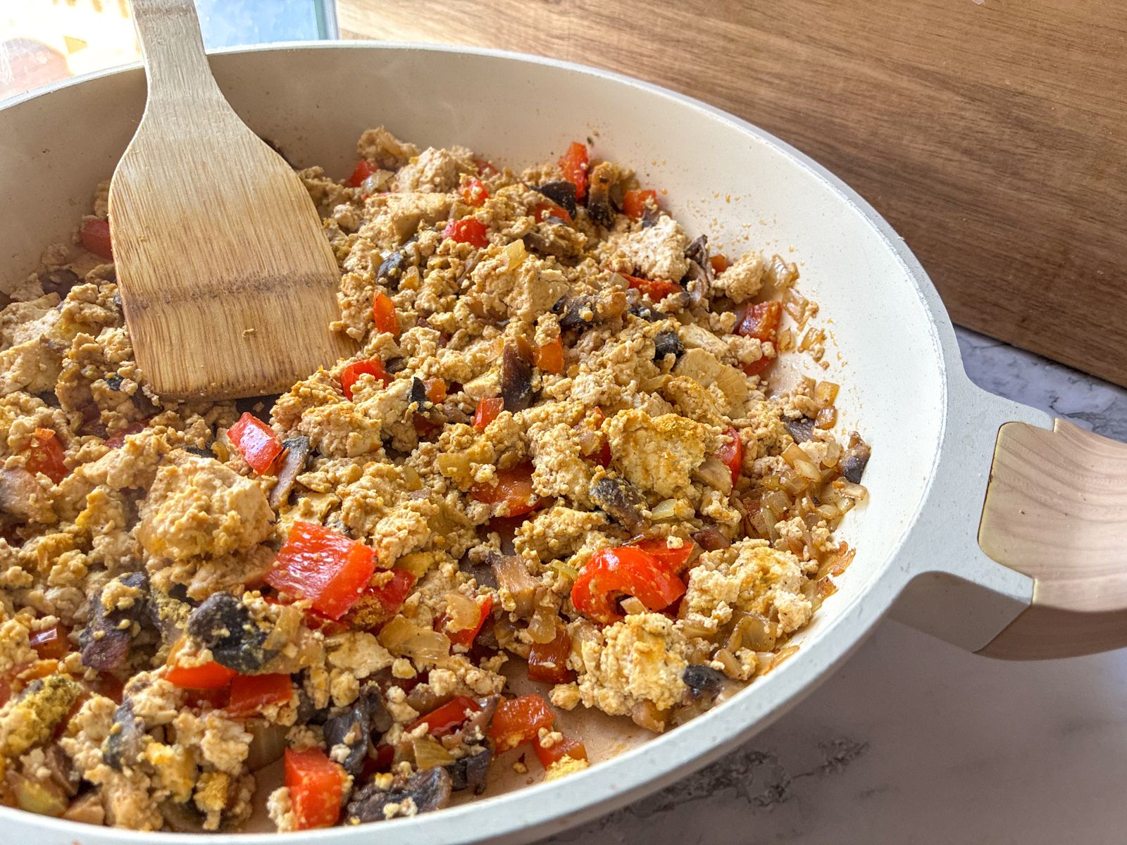 Tofu scramble with mushrooms and peppers in a large skillet with a serving spoon