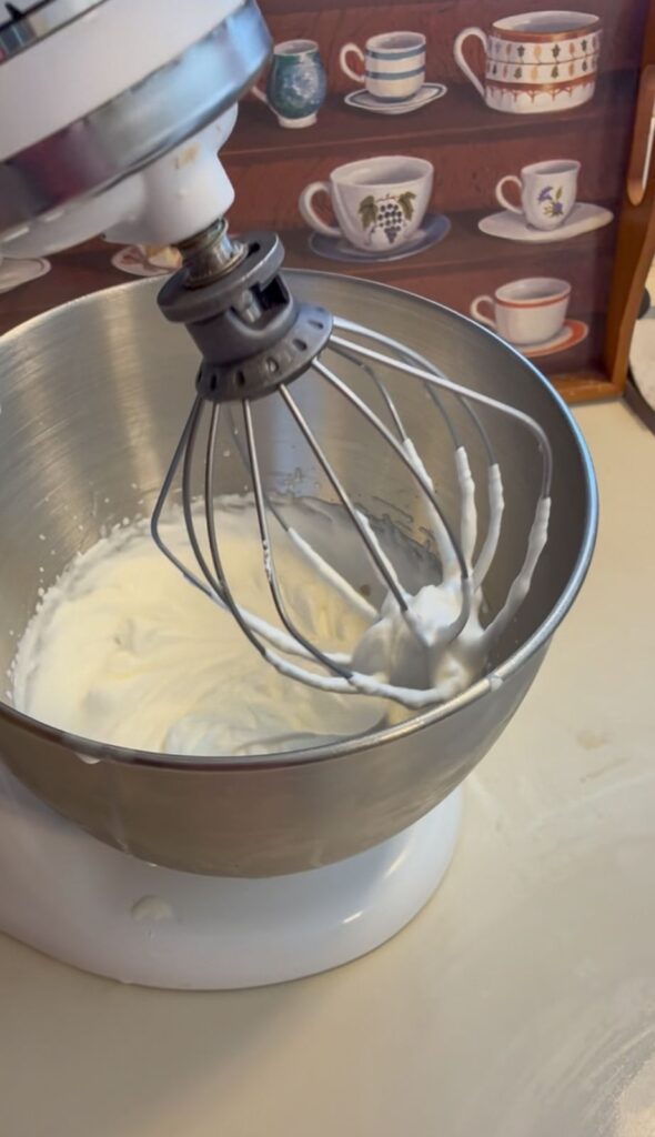 stand mixer with whisk attachment having whipped cream on it