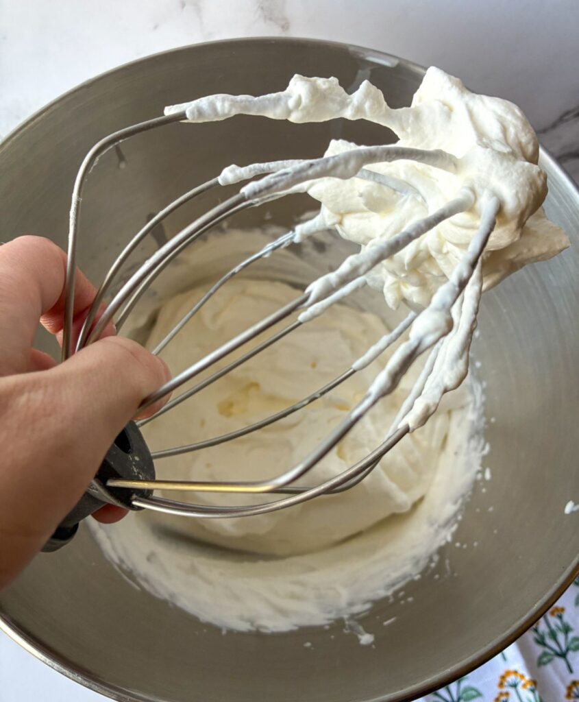 2 ingredient whipped cream on a whisk held over the metal bowl