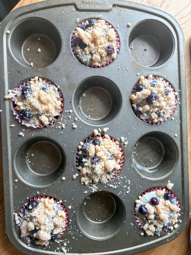6 batter filled muffin tins with a crumb topping for eggless lemon blueberry muffins