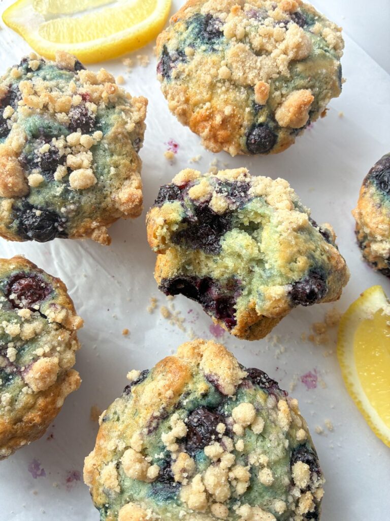6 eggless lemon blueberry muffins one with a bite taken out of it