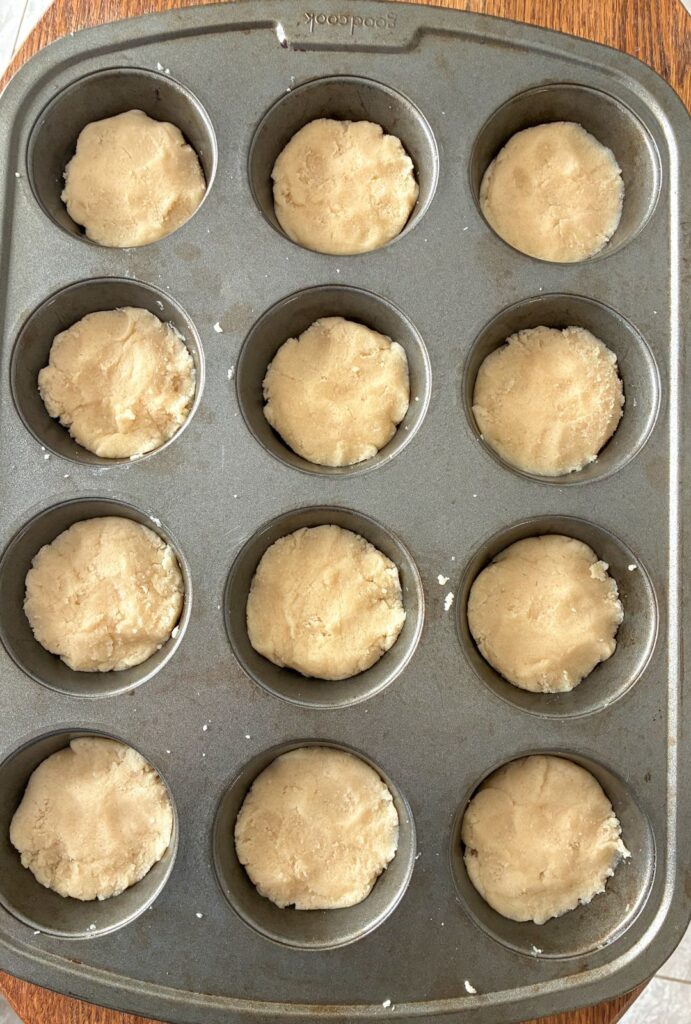 eggless sugar cookie dough divided into 12 muffin tin cups and press down flat prior to baking