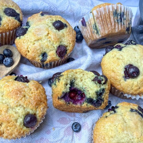 7 eggless blueberry muffins and a bowl of blueberries on a table