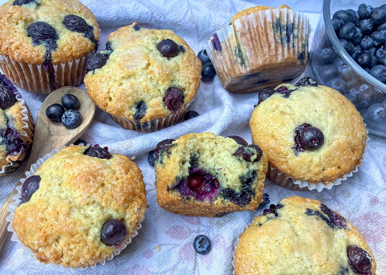 7 eggless blueberry muffins and a bowl of blueberries on a table