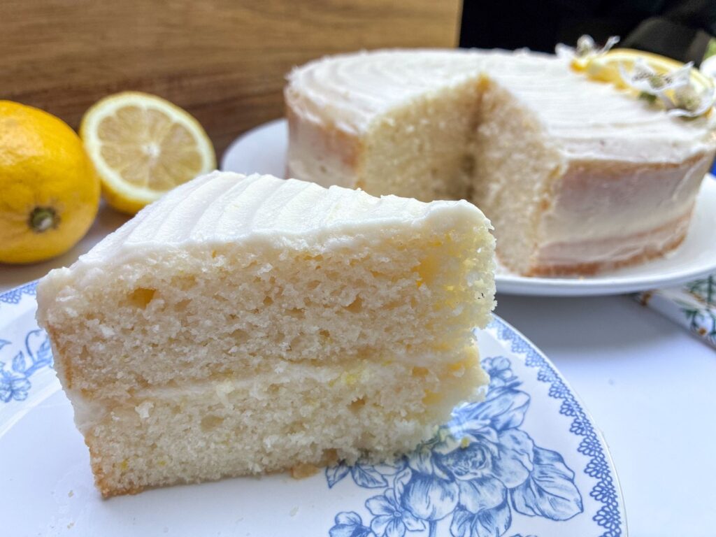 Slice of eggless lemon cake on a plate in front of the full cake