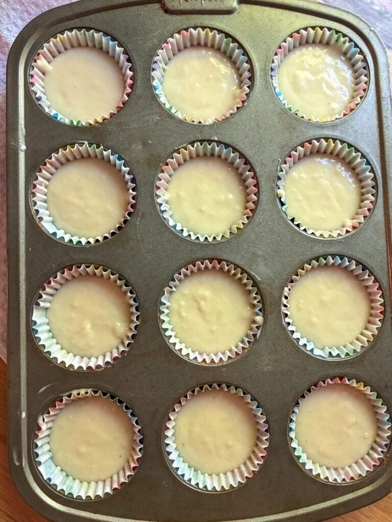 A 12-tin muffin pan with cupcake liners filled 2/3 of the way full of batter for eggless vanilla cupcakes