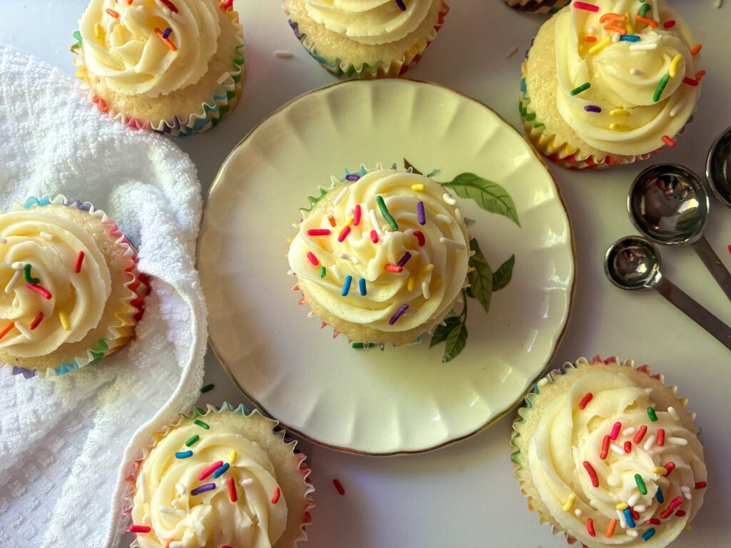 7 eggless vanilla cupcakes with one of them on a plate