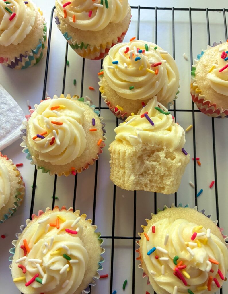 Eggless vanilla cupcakes on a cooling wrack with a bite taken out of one of them