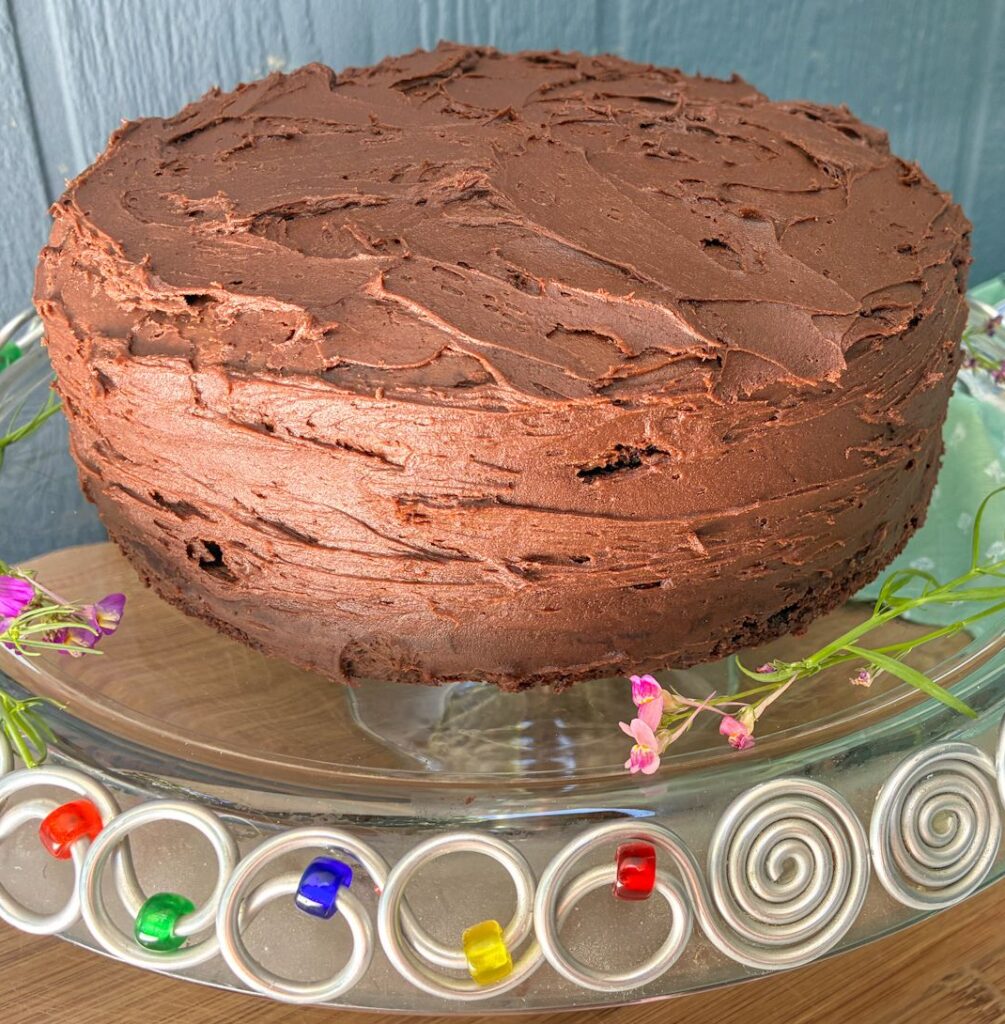 Eggless chocolate cake that is completely frosted and on a cake stand