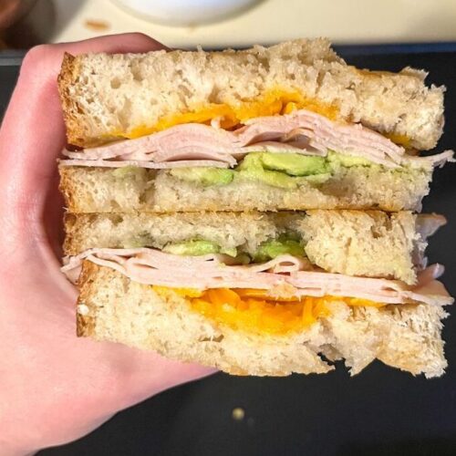 sourdough turkey melt cut in half and being held in a hand above a griddle