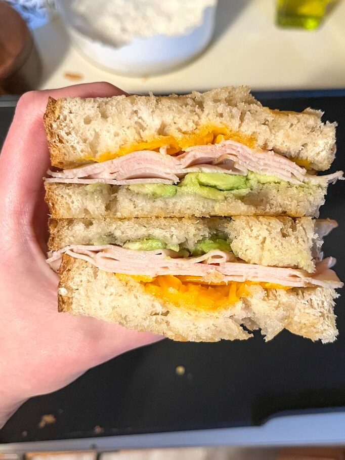 sourdough turkey melt cut in half and being held in a hand above a griddle