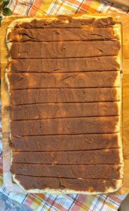 eggless cinnamon roll dough rolled out with brown sugar on top and strips cut out
